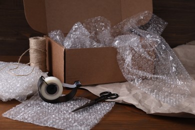 Photo of Bubble wrap, adhesive tape, twine and scissors near cardboard box on wooden table