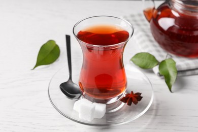 Photo of Glass of traditional Turkish tea and sugar cubes on white wooden table, closeup