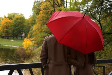 Photo of Couple with red umbrella in autumn park, back view. Space for text
