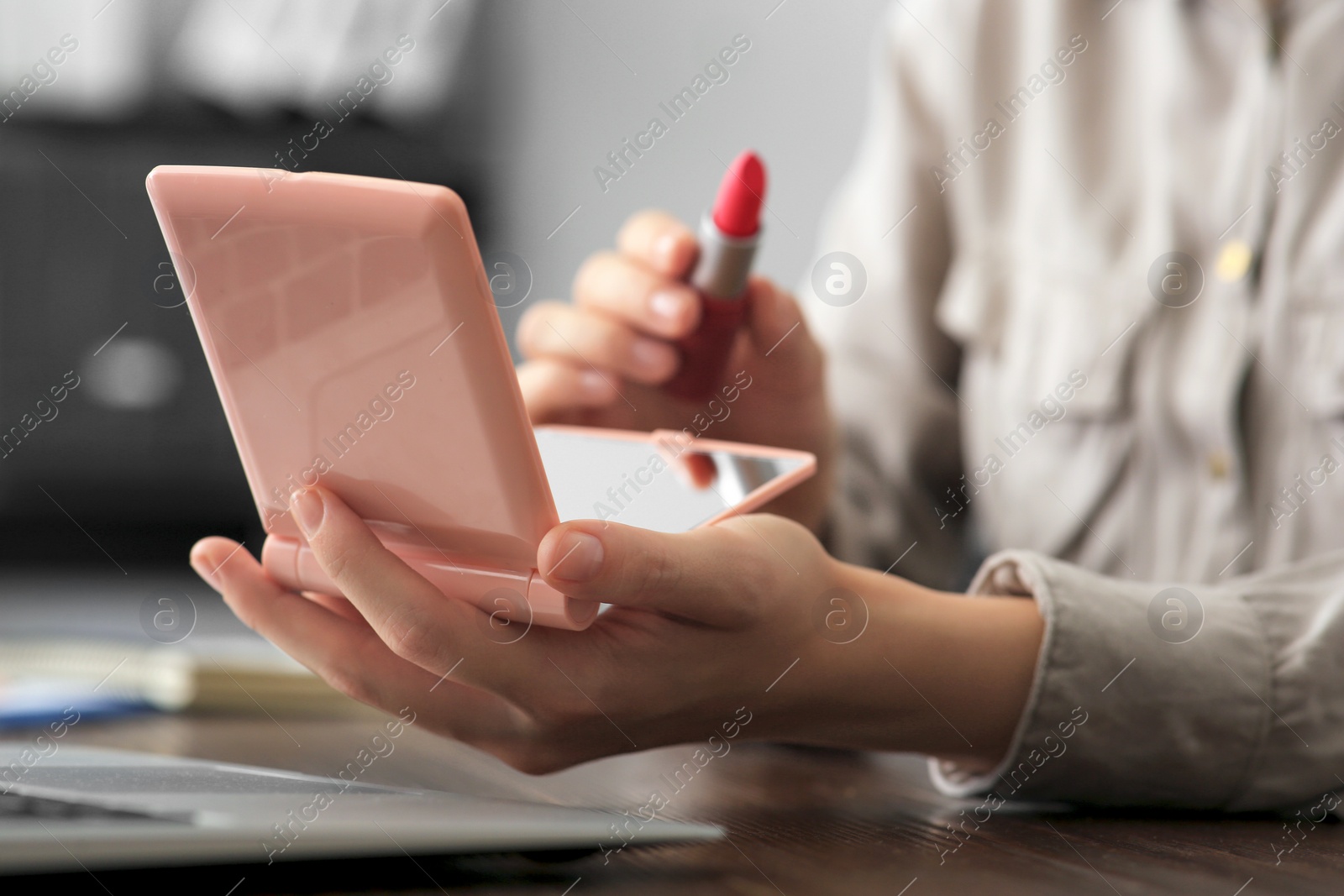 Photo of Woman with cosmetic pocket mirror and lipstick at wooden table indoors, closeup