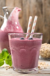 Photo of Glass of blackberry smoothie with straws, mint and oatmeal on light wooden table