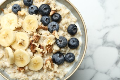 Photo of Tasty oatmeal with banana, blueberries, walnuts and milk served in bowl on white marble table, top view