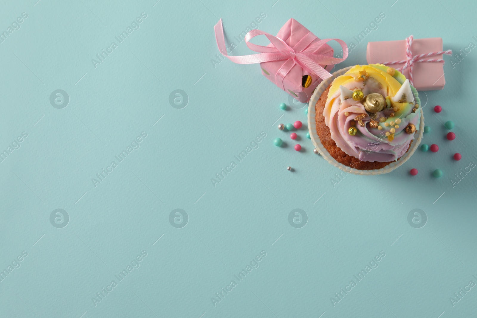 Photo of Cute sweet unicorn cupcake and gift boxes on light turquoise background, top view. Space for text