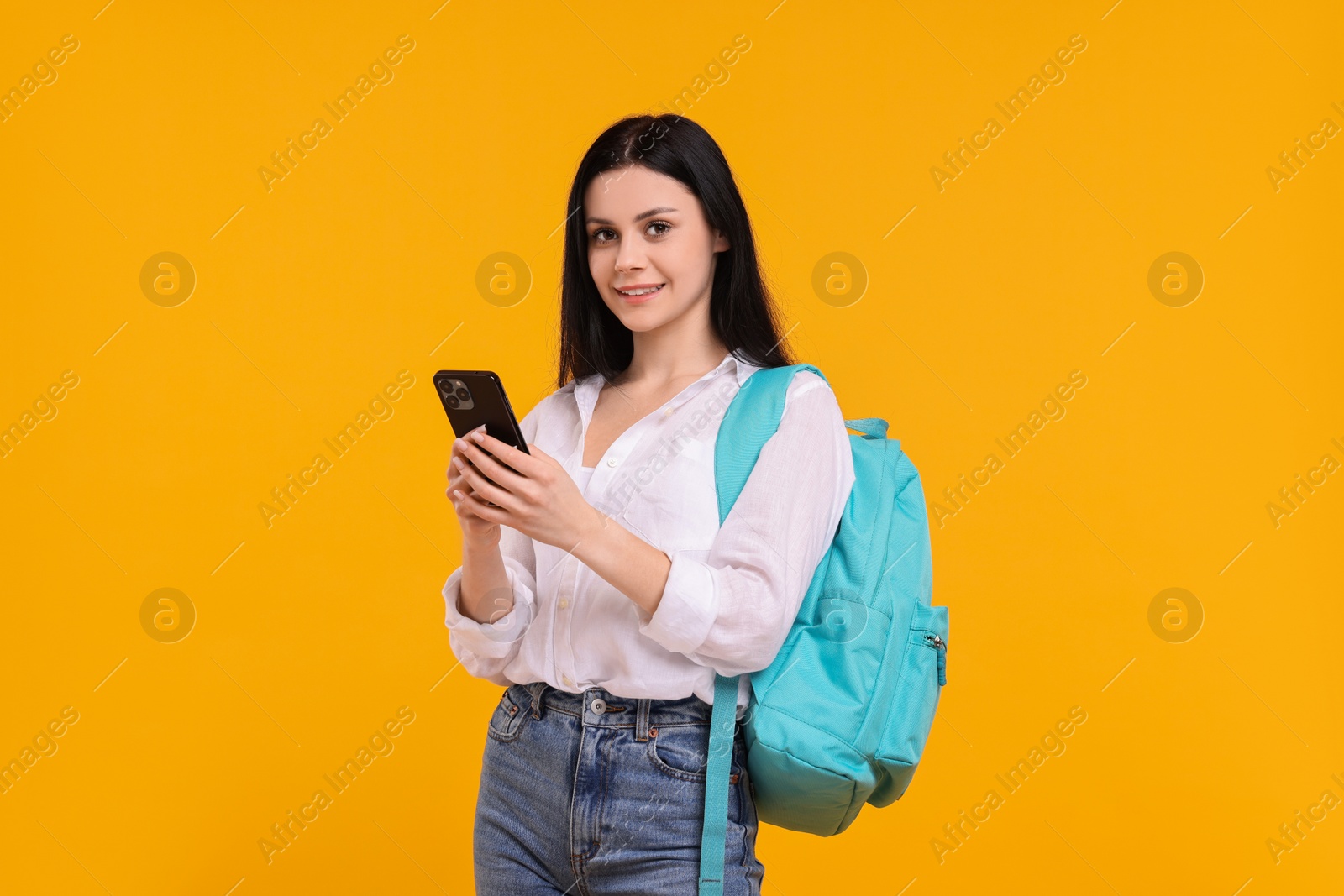 Photo of Smiling student with smartphone on yellow background