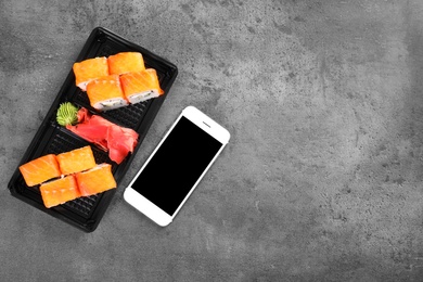 Tasty sushi rolls and smartphone with space for text on grey table, top view. Food delivery