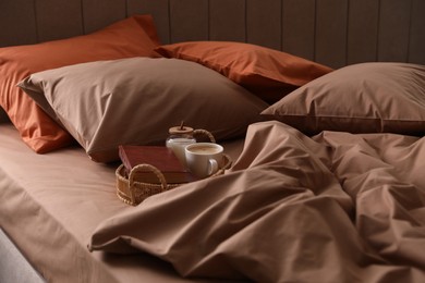 Cup of hot coffee and books on bed with stylish linens