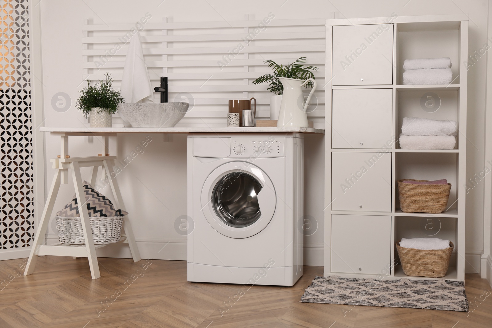 Photo of Laundry room interior with modern washing machine and shelving unit near white wall