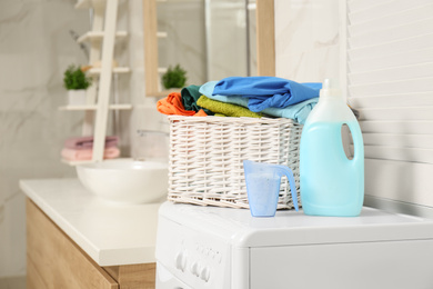 Photo of Wicker basket with laundry and detergents on washing machine in bathroom