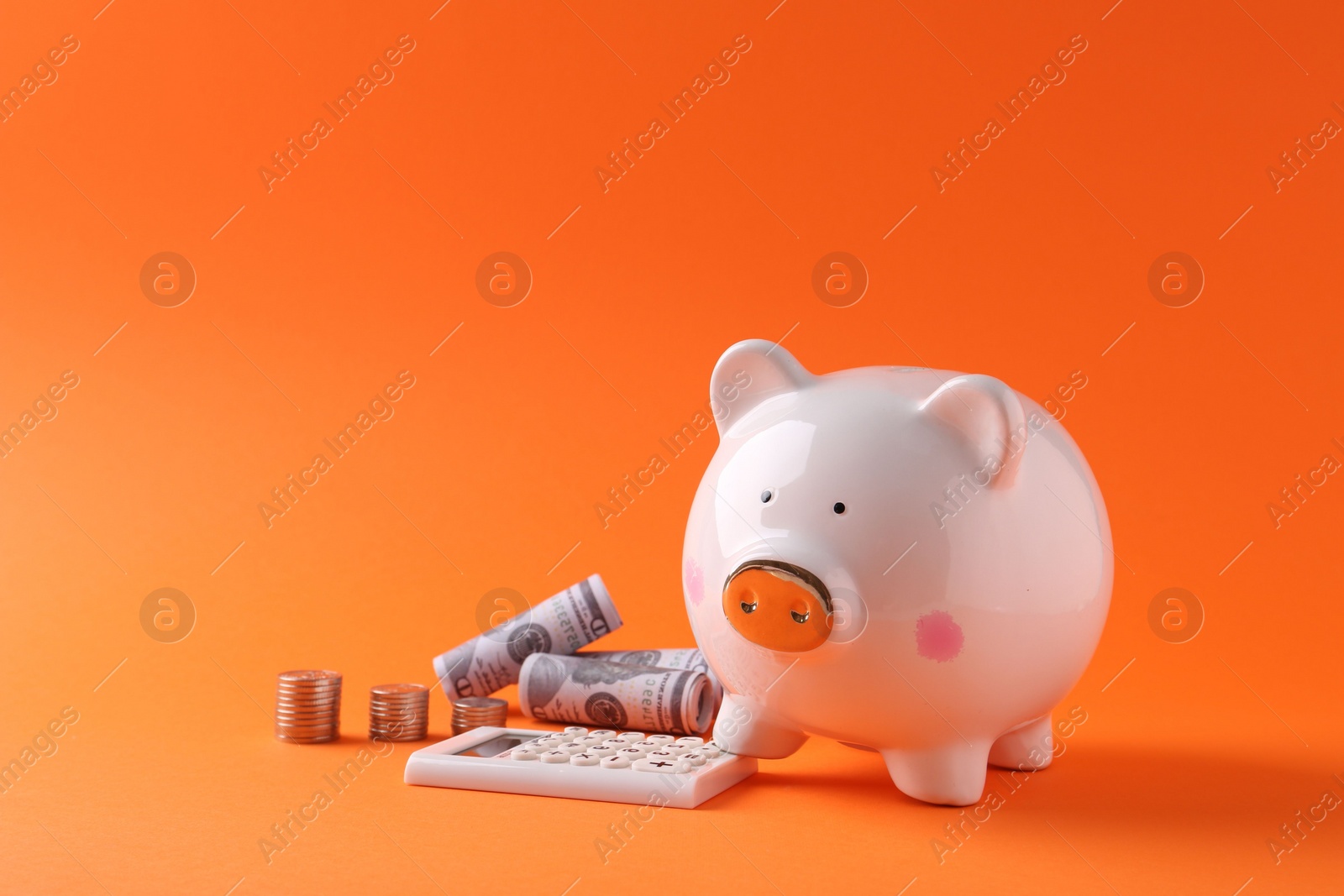 Photo of Financial savings. Piggy bank, dollar banknotes, coins and calculator on orange background