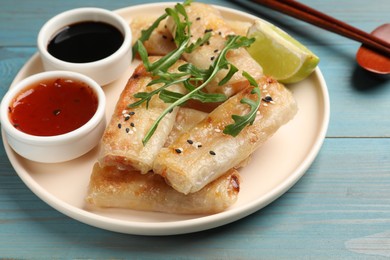 Photo of Tasty fried spring rolls served on light blue wooden table, closeup