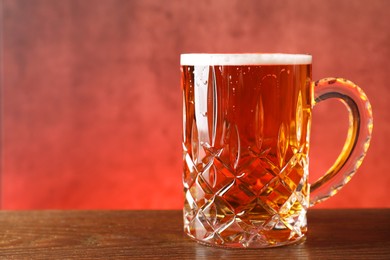 Mug with fresh beer on wooden table against pink background, closeup. Space for text