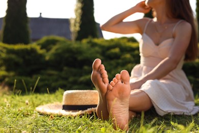 Woman sitting barefoot on green grass outdoors, closeup. Space for text