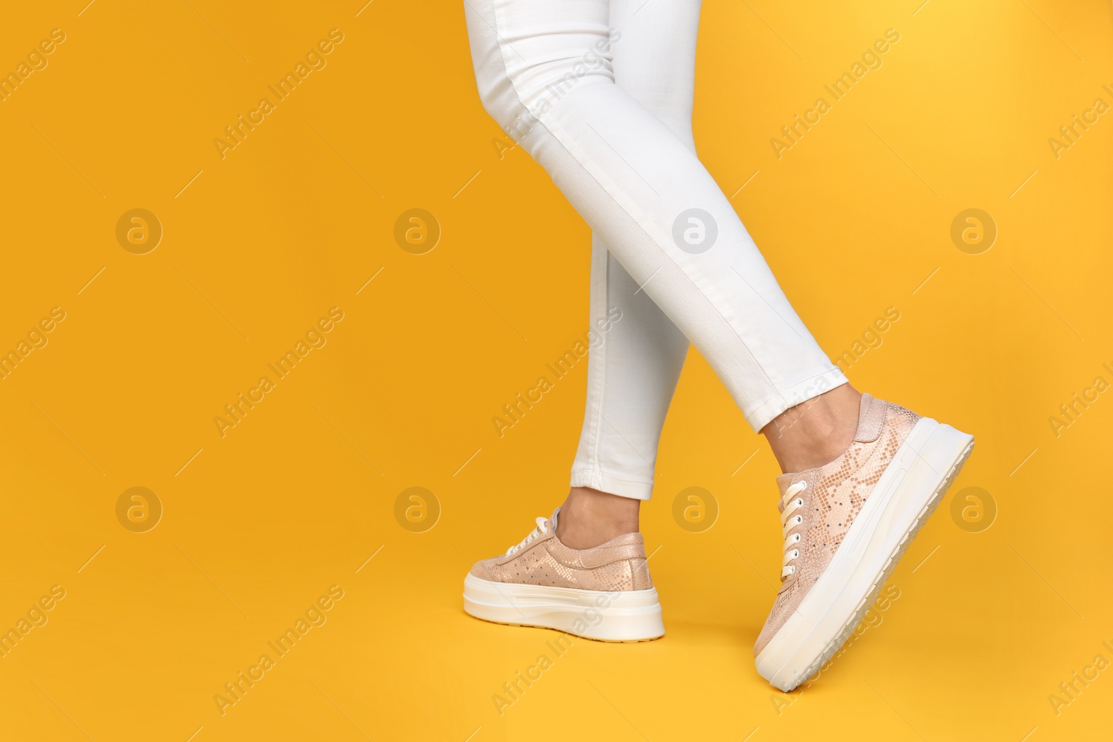 Photo of Woman wearing stylish shoes on yellow background, closeup. Space for text