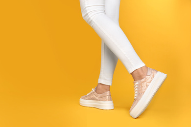 Photo of Woman wearing stylish shoes on yellow background, closeup. Space for text