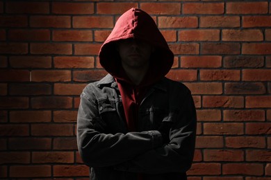 Photo of Thief in hoodie with crossed arms against red brick wall