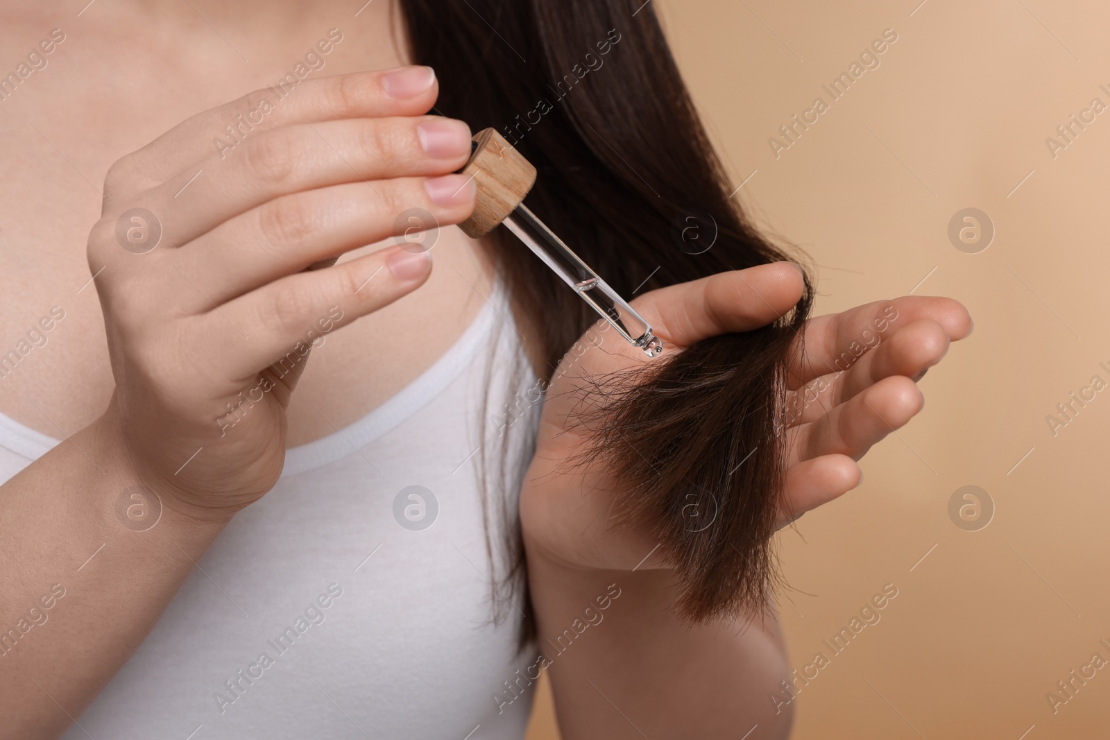 Photo of Woman applying essential oil onto hair on beige background, closeup