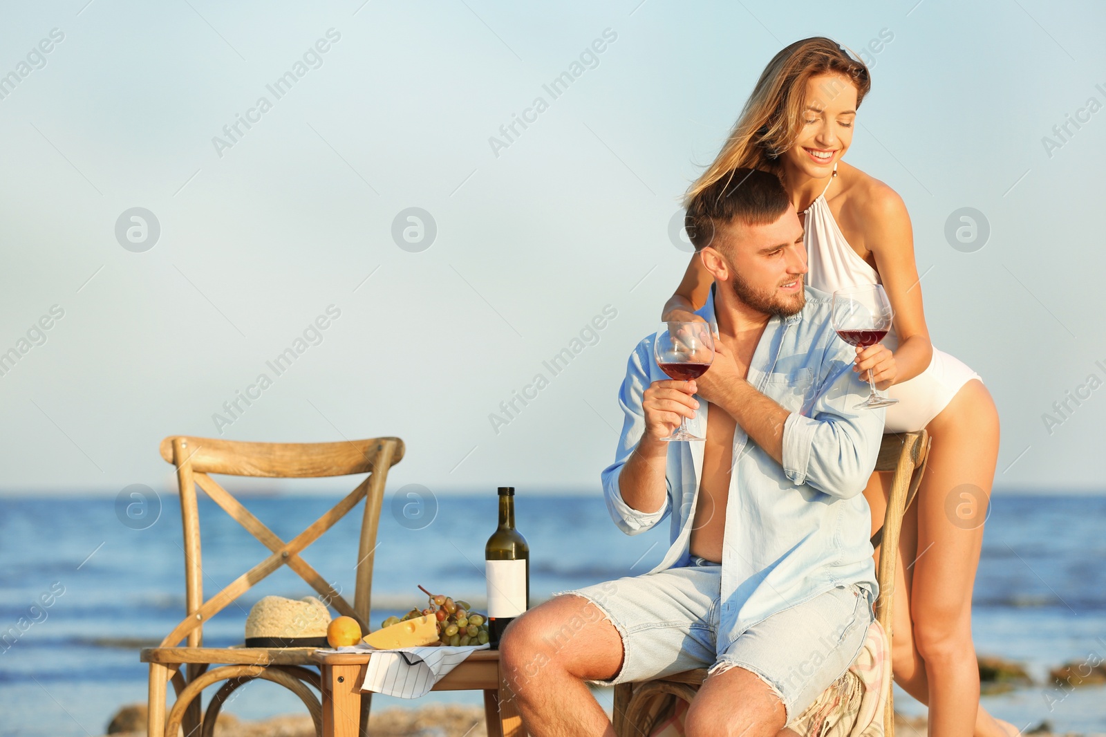 Photo of Young couple with glasses of wine having romantic dinner on beach