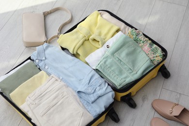 Open suitcase packed for trip, handbag and shoes on floor