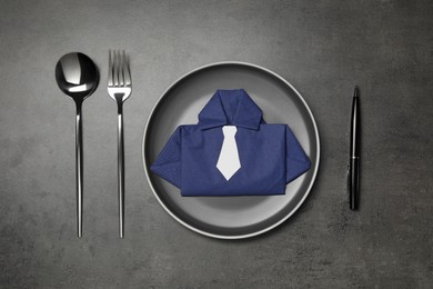 Photo of Plate with shirt made of paper napkin, cutlery and pen on gray table, flat lay. Business lunch concept