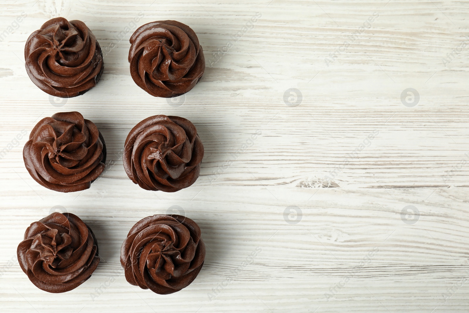 Photo of Delicious chocolate cupcakes with cream on white wooden table, flat lay. Space for text