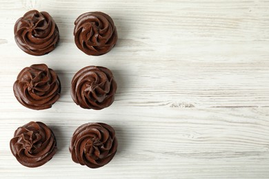 Delicious chocolate cupcakes with cream on white wooden table, flat lay. Space for text