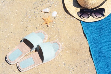 Photo of Stylish slippers, straw hat, sunglasses and blue towel on sand. Beach accessories