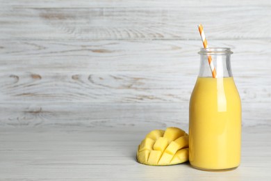 Photo of Bottle of tasty smoothie with straw and mango on white wooden table. Space for text