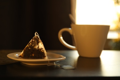 Photo of Saucer with used pyramid tea bag on table. Space for text