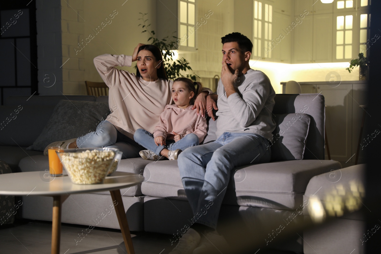 Photo of Family watching movie with popcorn on sofa at night