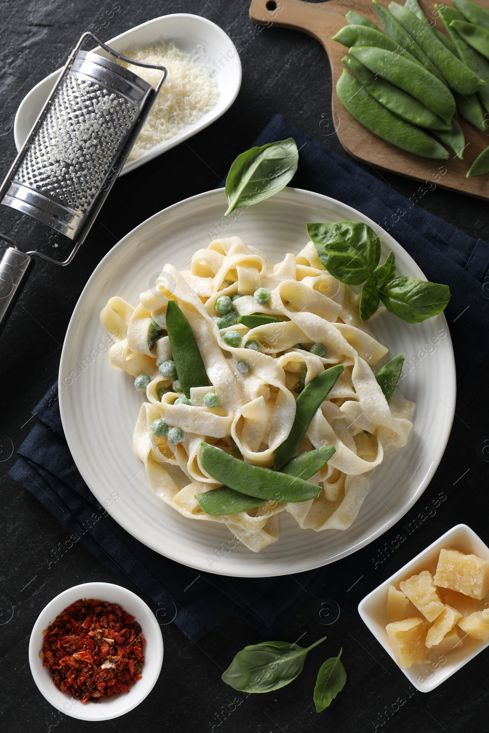 Photo of Delicious pasta with green peas and ingredients on black table, flat lay