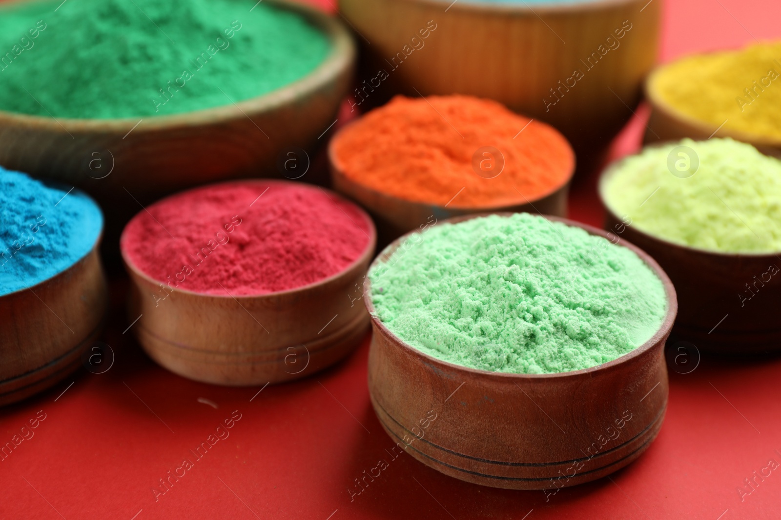 Photo of Colorful powders in wooden bowls on red background. Holi festival celebration