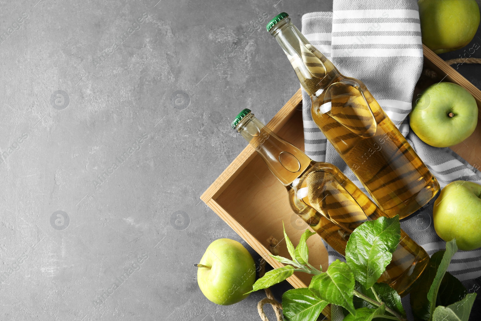 Photo of Delicious cider, ripe apples and green leaves on gray table, flat lay. Space for text