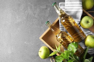 Delicious cider, ripe apples and green leaves on gray table, flat lay. Space for text