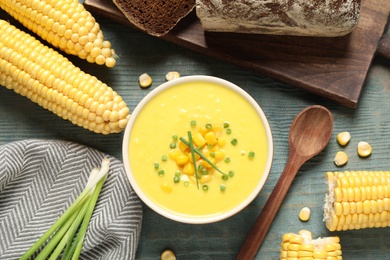 Photo of Delicious creamy corn soup served on blue wooden table, flat lay