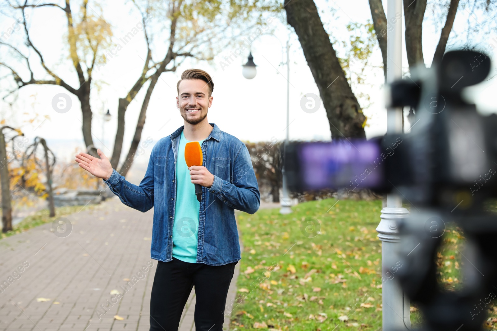 Photo of Young male journalist with microphone working in park