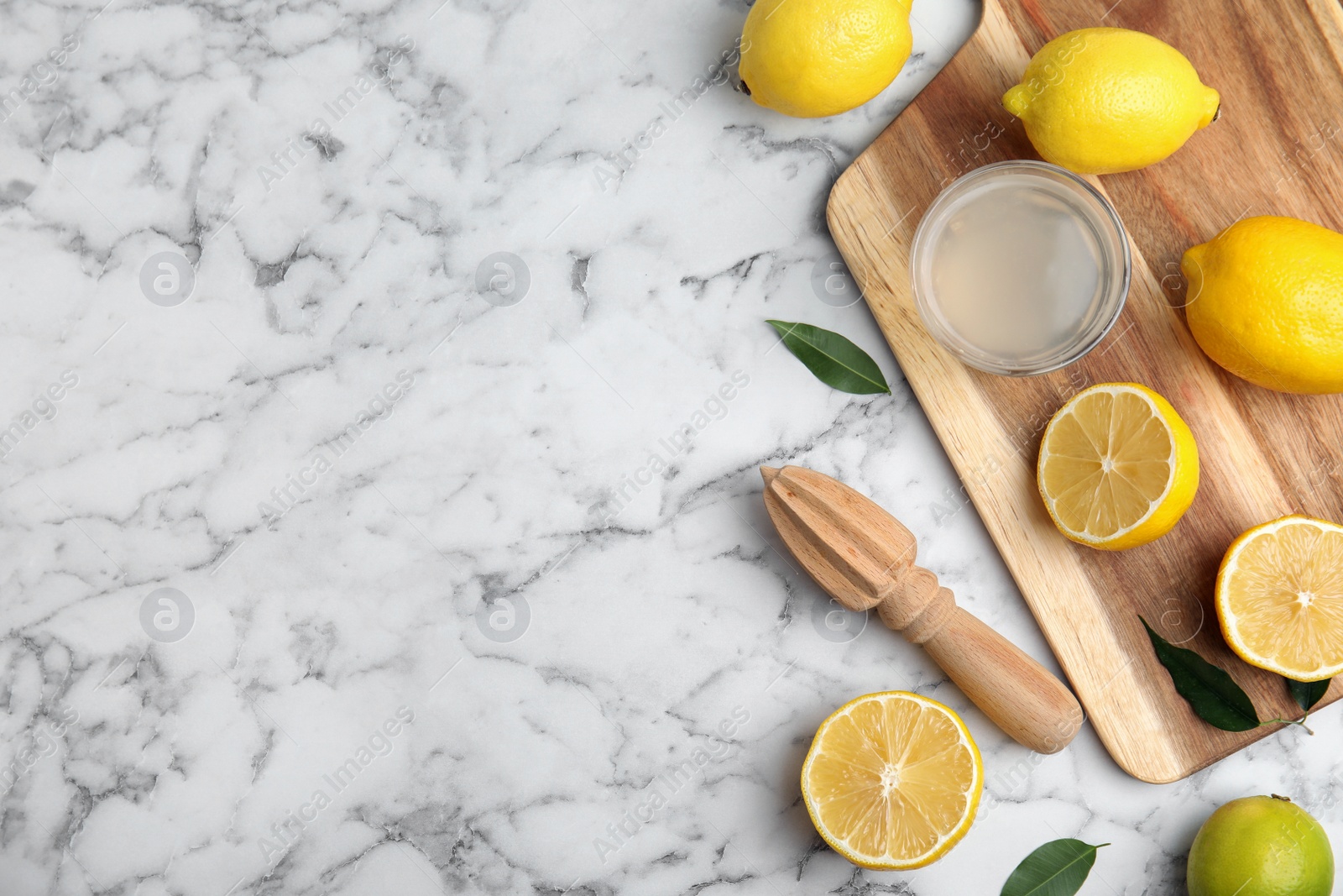 Photo of Wooden citrus reamer, juice, fresh lemons and lime on white marble table, flat lay. Space for text