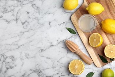 Wooden citrus reamer, juice, fresh lemons and lime on white marble table, flat lay. Space for text