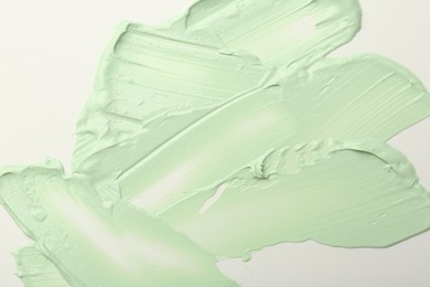 Photo of Strokes of green color correcting concealer on white background, top view