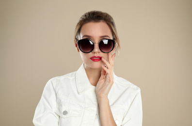 Young woman wearing stylish sunglasses on beige background