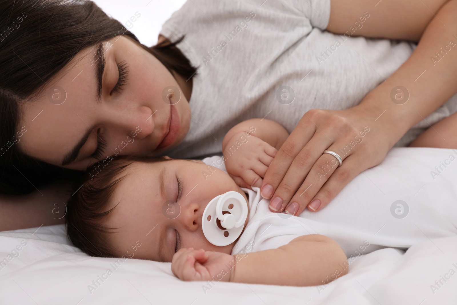 Photo of Young mother resting near her sleeping baby on bed, closeup