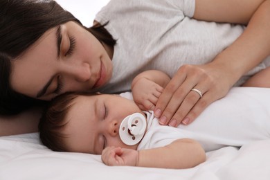 Photo of Young mother resting near her sleeping baby on bed, closeup