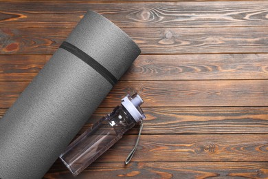 Photo of Yoga mat and bottle of water on wooden floor, flat lay. Space for text