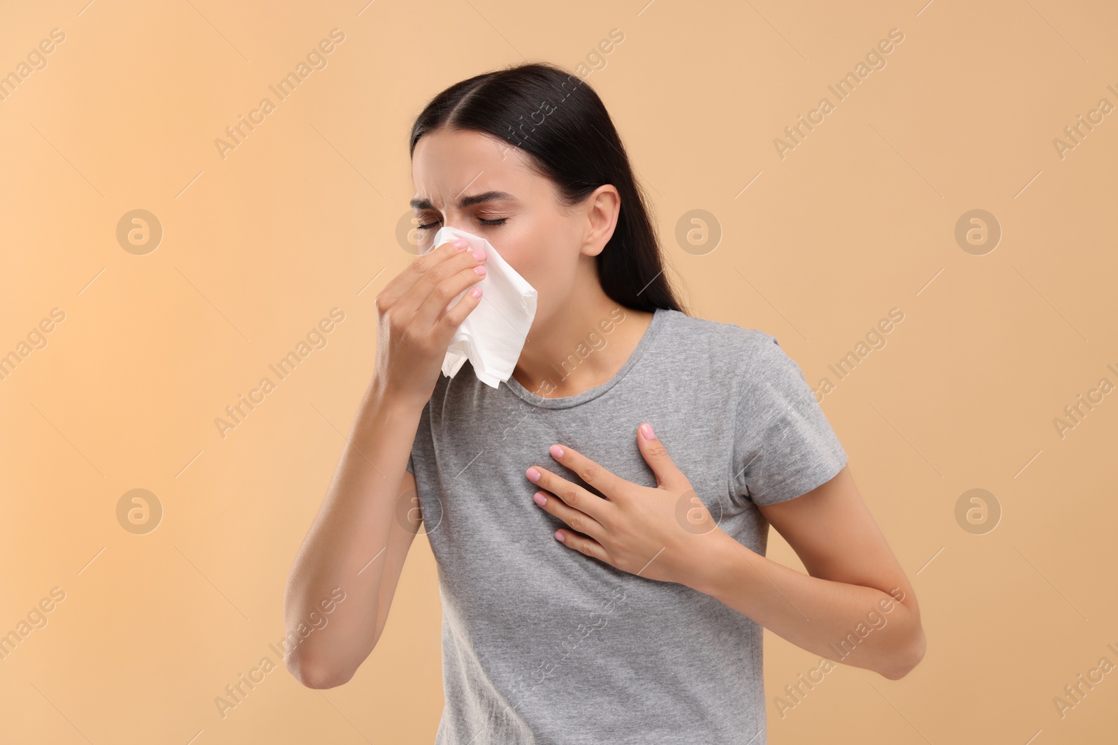Photo of Suffering from allergy. Young woman blowing her nose in tissue on beige background