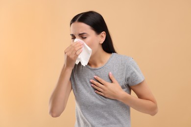 Suffering from allergy. Young woman blowing her nose in tissue on beige background