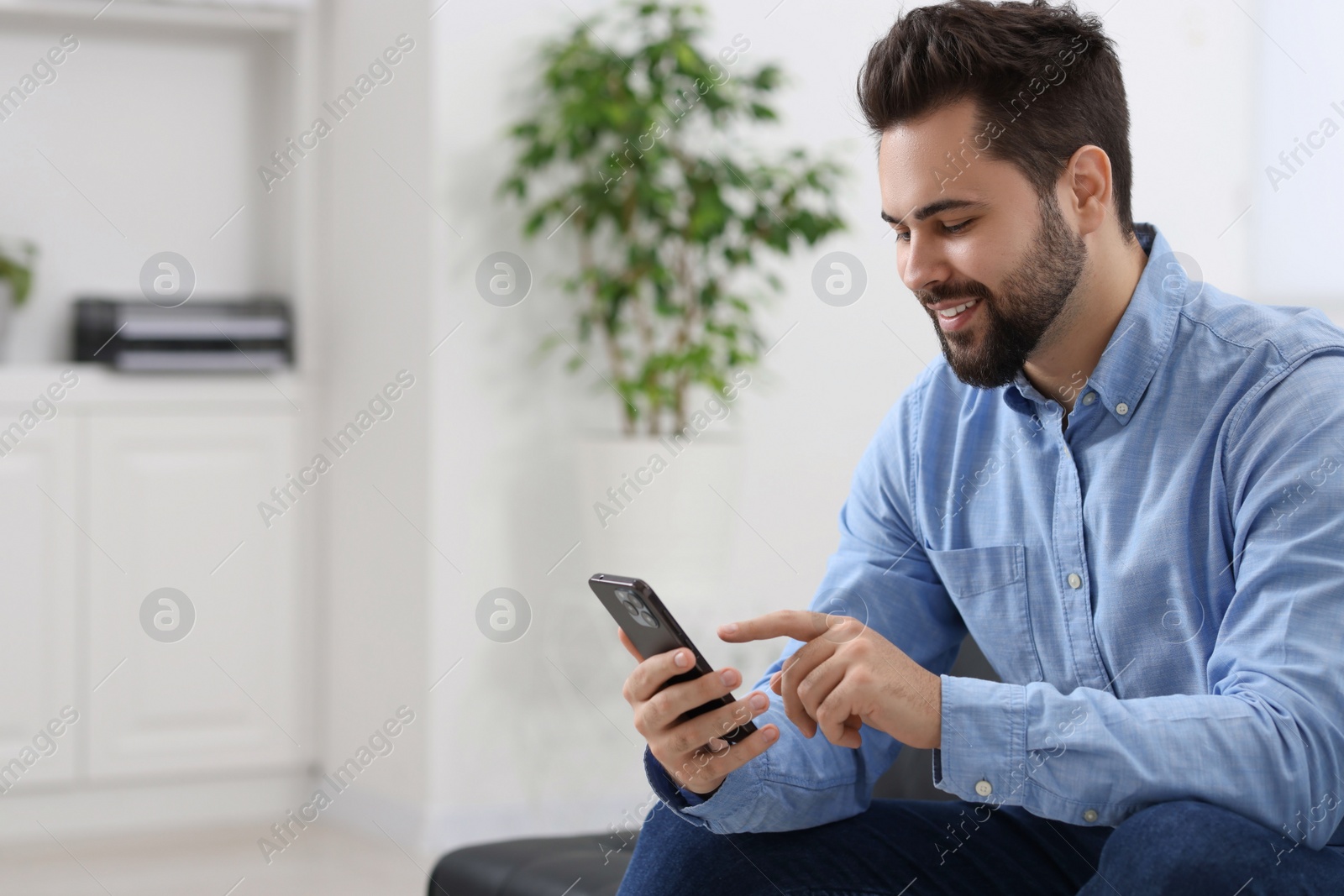 Photo of Handsome young man using smartphone in office, space for text