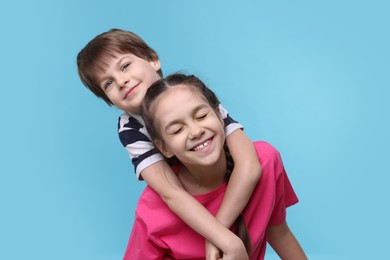 Happy brother and sister hugging on light blue background