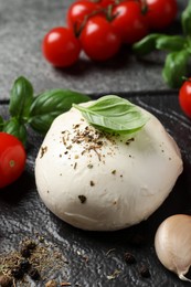 Photo of Delicious mozzarella with tomatoes and basil leaves on black table, closeup