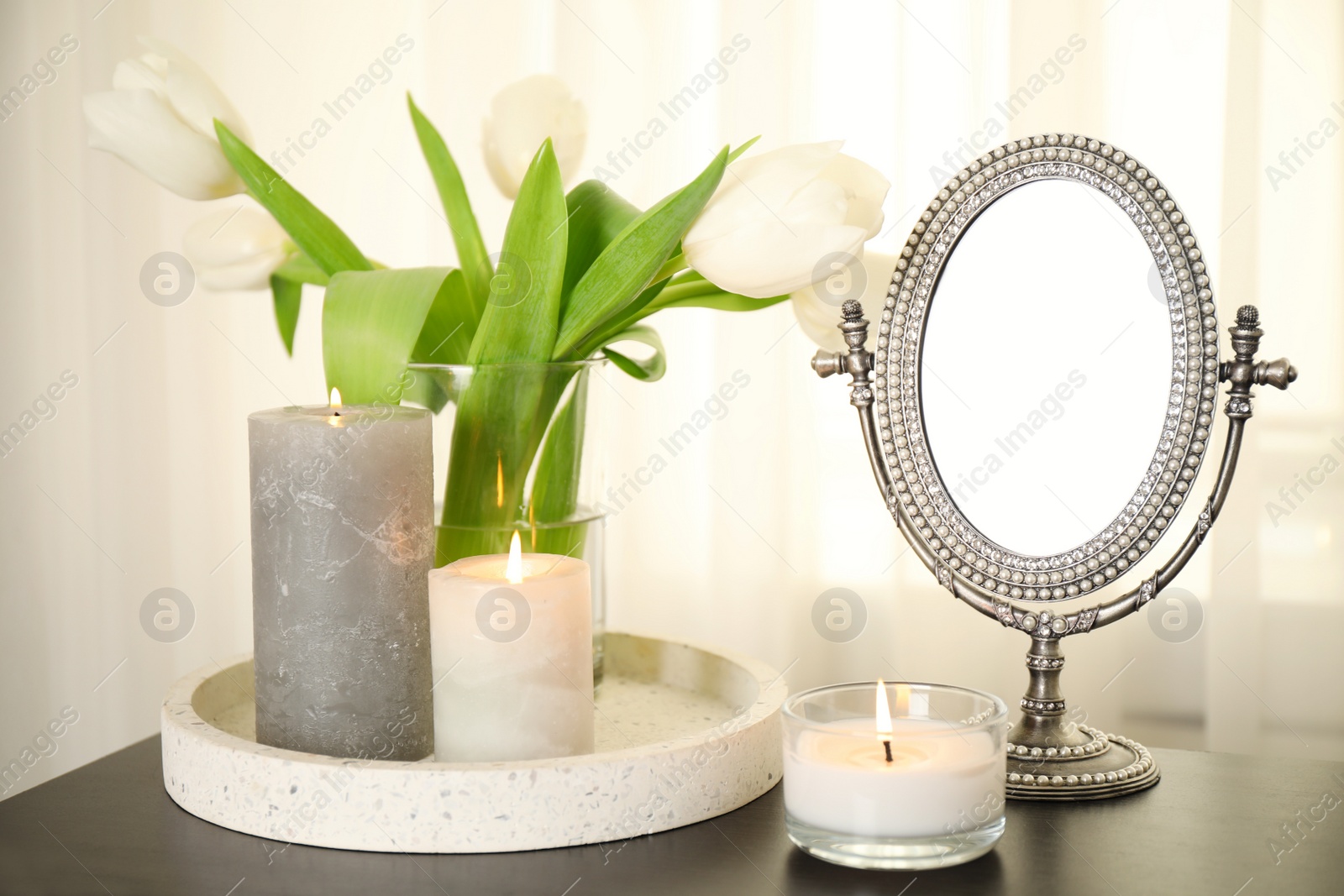 Photo of Burning candles, mirror and flowers on black table indoors
