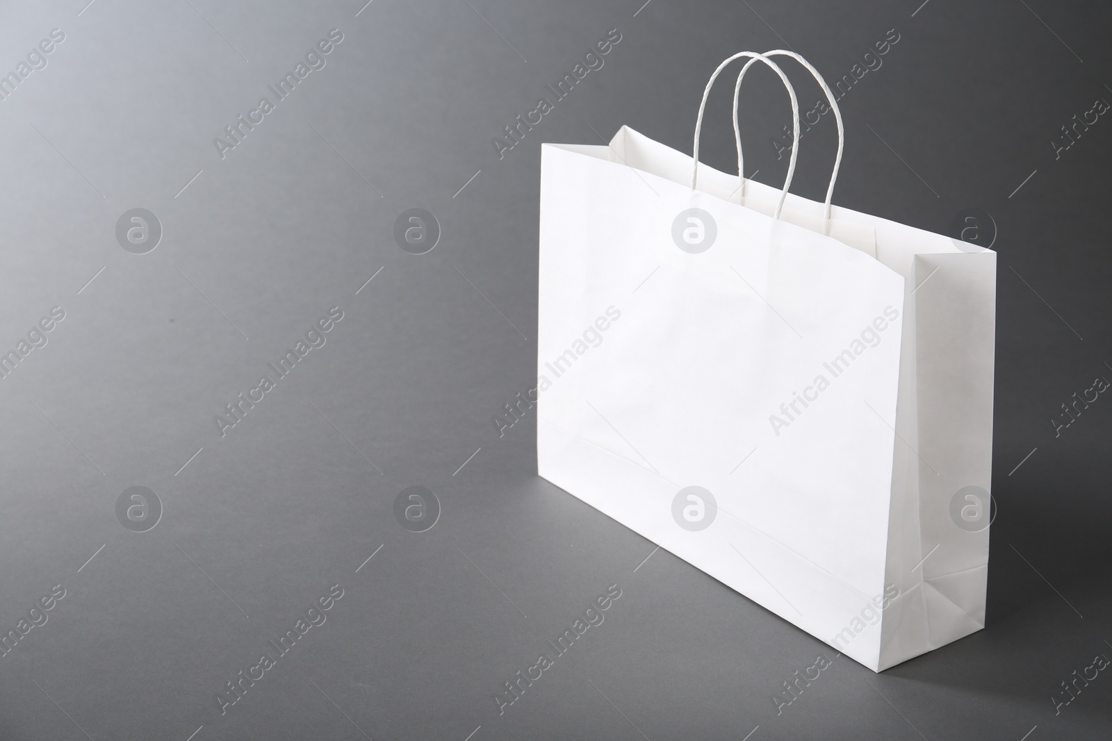 Photo of One white paper bag on grey background, space for text. Mockup for design