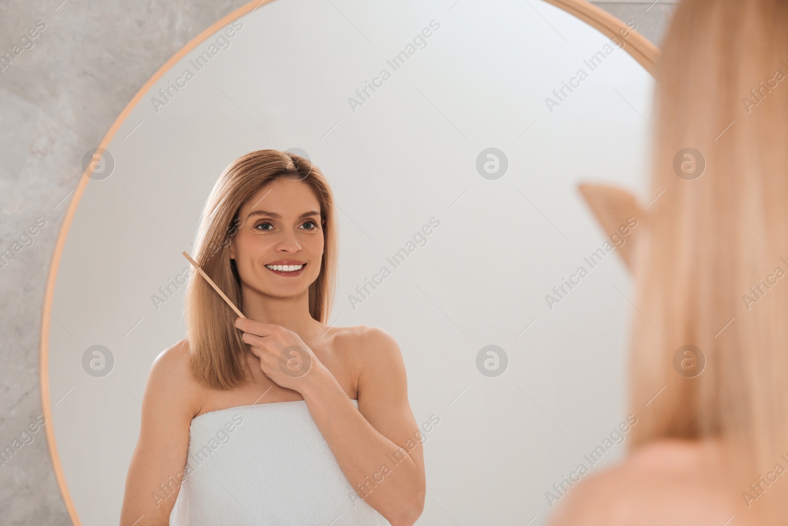 Photo of Beautiful woman brushing her hair near mirror in bathroom